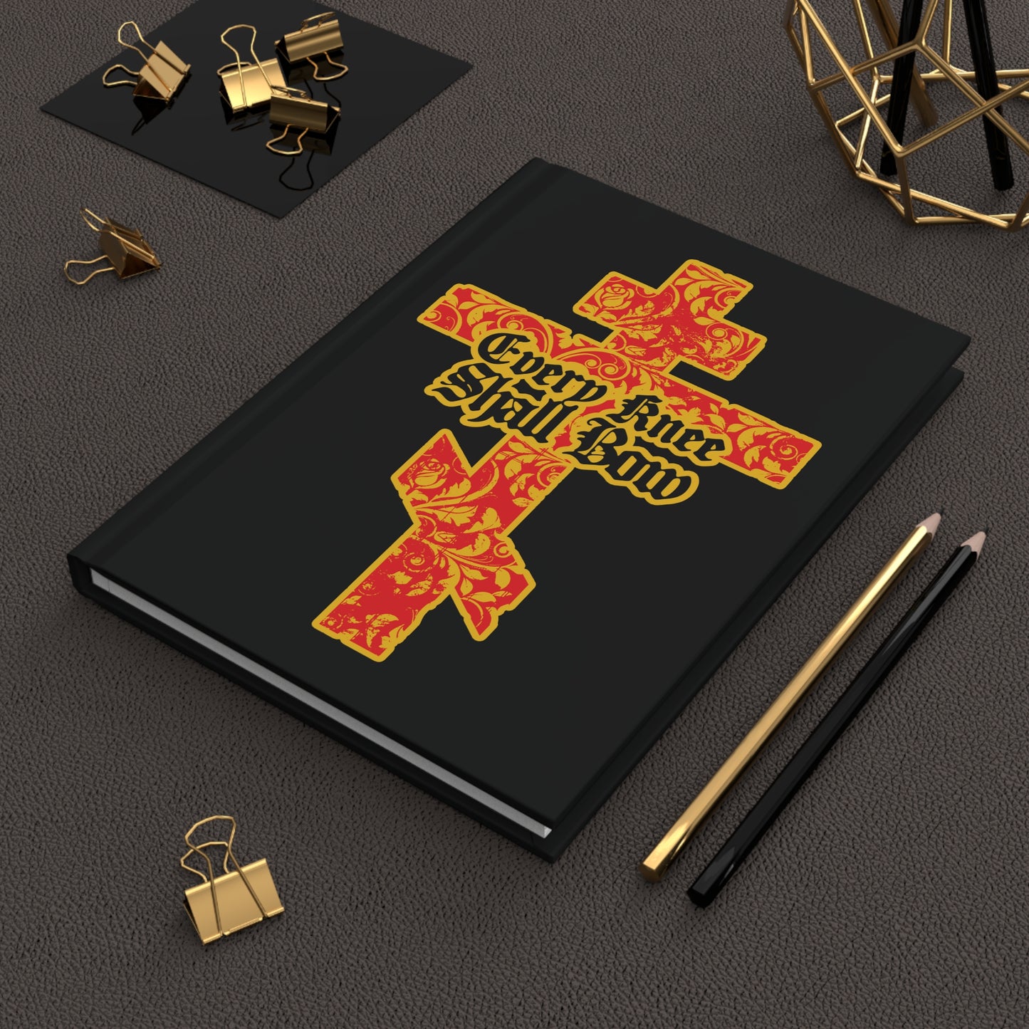 The "Every Knee Shall Bow" Christian Journal features a gold and red floral Orthodox cross with Gothic lettering (Isaiah 45:22-24, Phil 2:7-11) on a black cover, perfect for your desk or stationery collection.