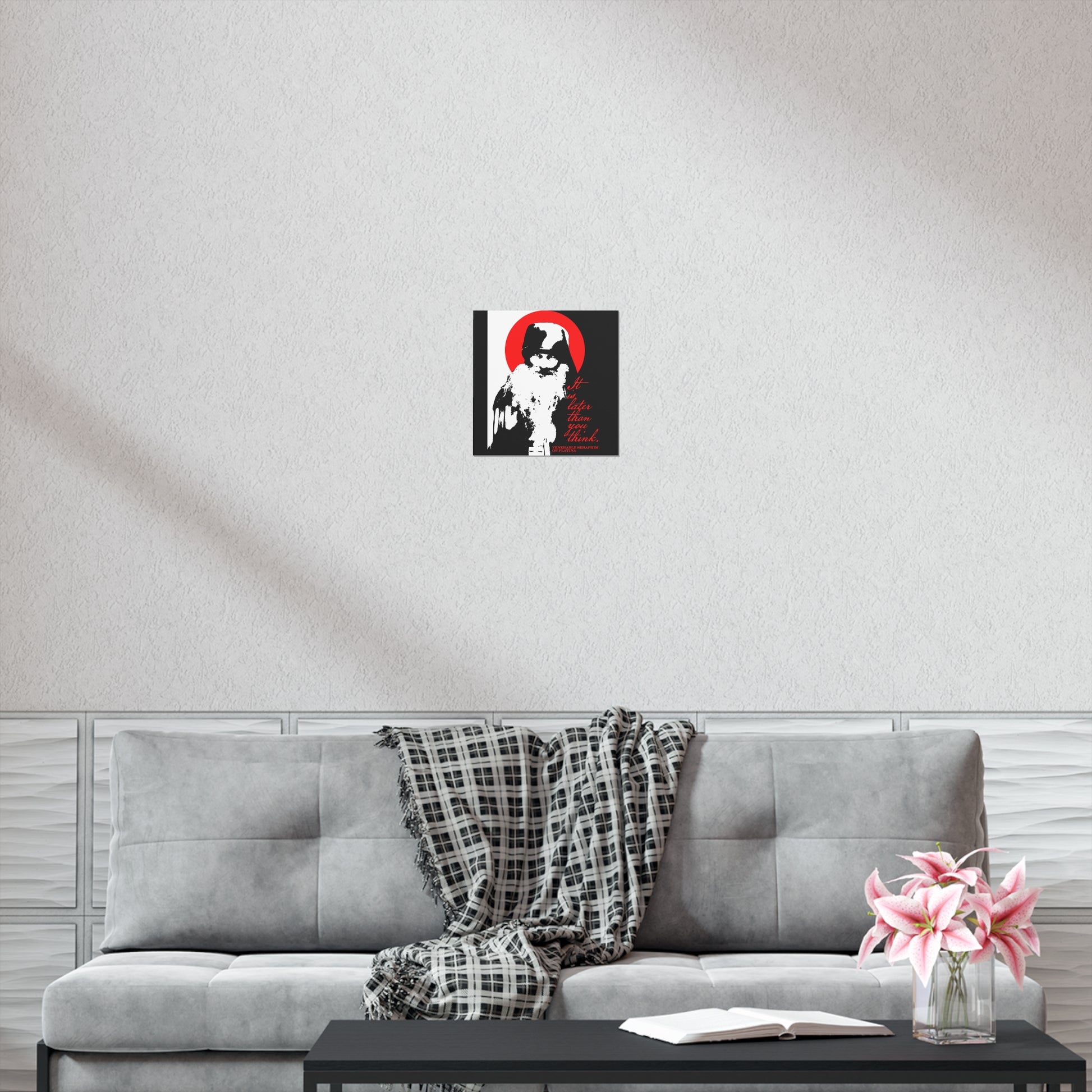 A modern living room with a gray sofa, plaid throw blanket, coffee table with an open "It's Later Than You Think" Orthodox book, pink flowers, and Remembrance of Death black, white, and red Christian art poster on the light-colored wall above the sofa.