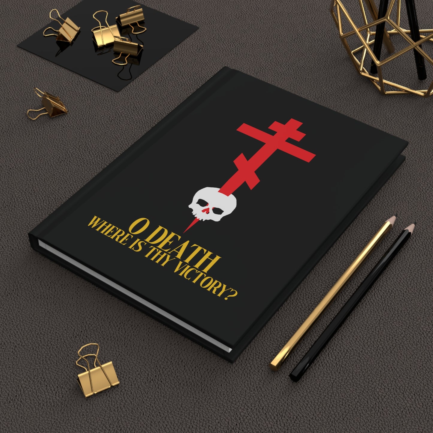 The "O Death Where is Thy Victory?" (1 Corinthians 15:55) hardcover journal features a cross stabbing a skull and yellow text—a unique Orthodox Christian accessory—displayed on a desk with stationery items.