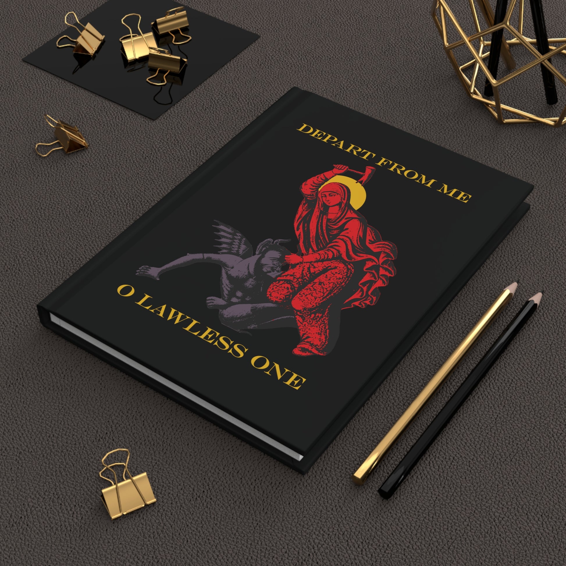 The hardcover St Marina IconoGraphic Journal—featuring "Depart from Me O Lawless One" and a red angelic figure, inspired by the Life of Saint Marina—sits on a desk with stationery.