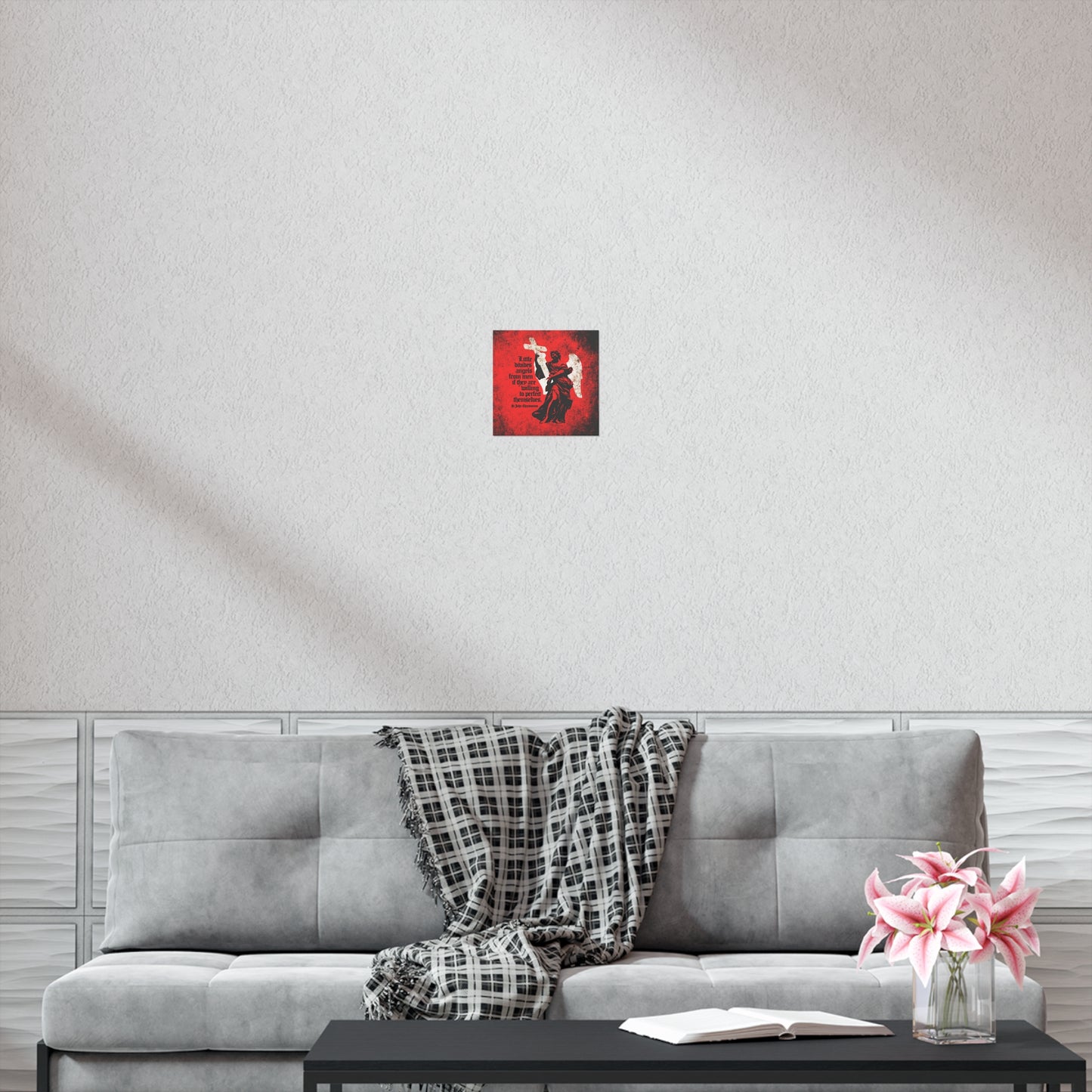 A gray sofa with a plaid throw, a book and flowers on a black table, and the "Little Divides Angels from Men" Christian Perfection art poster by St. John Chrysostom create a peaceful space for reflection.