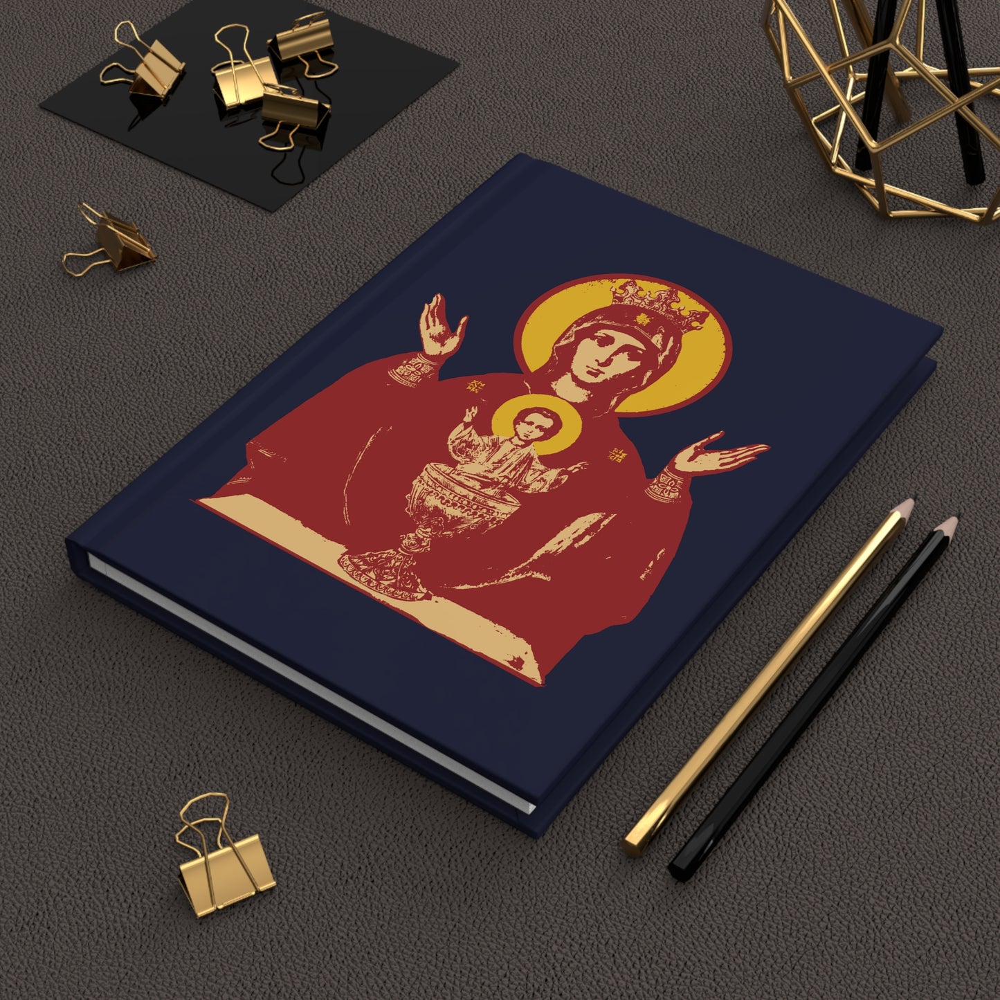 A navy blue Orthodox Christian blank journal featuring the Holy Theotokos IconoGraphic of the Inexhaustible Chalice, Deliverer from Addictions and Conqueror of Passions, displayed on a brown desk with stationery.