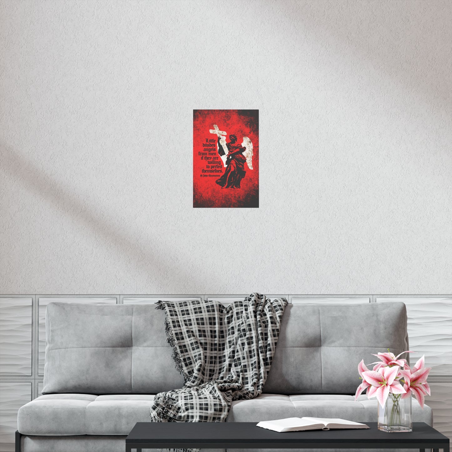 A gray couch with a plaid blanket, a book, and pink flowers sits beneath the "Little Divides Angels from Men | Christian Perfection | St John Chrysostom" Orthodox Christian Art Poster, creating a peaceful spot for reflection and grace.