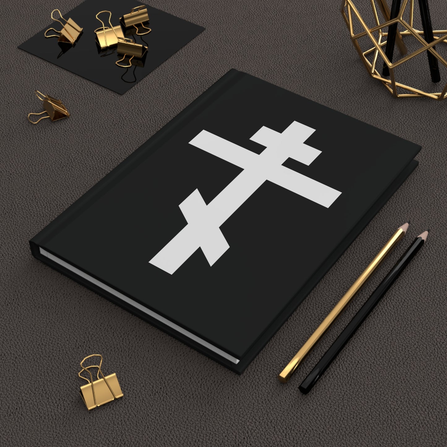 The "White Orthodox Cross | 'May I never boast, except in the cross of our Lord Jesus Christ' (Gal 6:14)" Orthodox Hardcover Journal features a white cross on a black cover, shown alongside gold clips and two pencils.