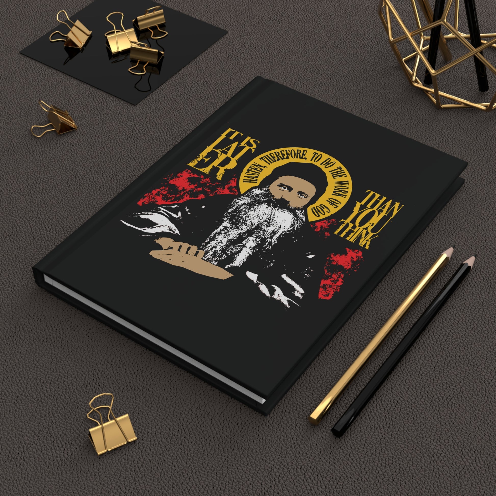 The "It's Later Than You Think (Fr Seraphim Rose) No. 13" Orthodox Christian hardcover journal, featuring a bearded man’s illustration and quote, rests on a desk with office supplies, echoing themes from Orthodox spiritual literature.