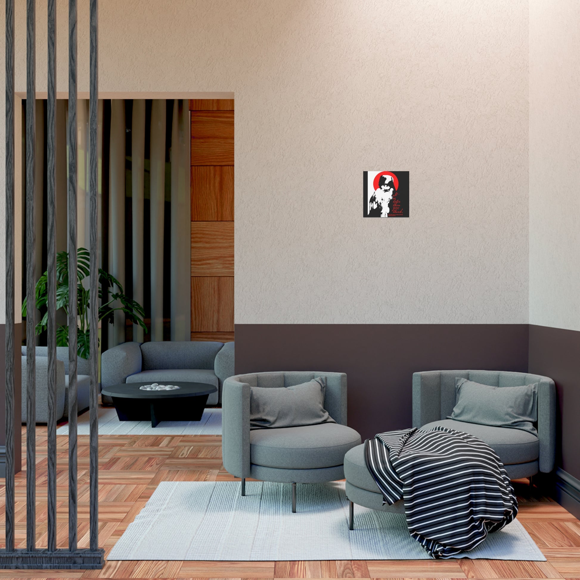 A modern lounge features two gray armchairs, a round table, and a striped blanket on a rug. Above hangs Remembrance of Death "It’s Later Than You Think" poster—black, white & red Christian art inspired by Fr Seraphim Rose. Another seating area appears in the background.