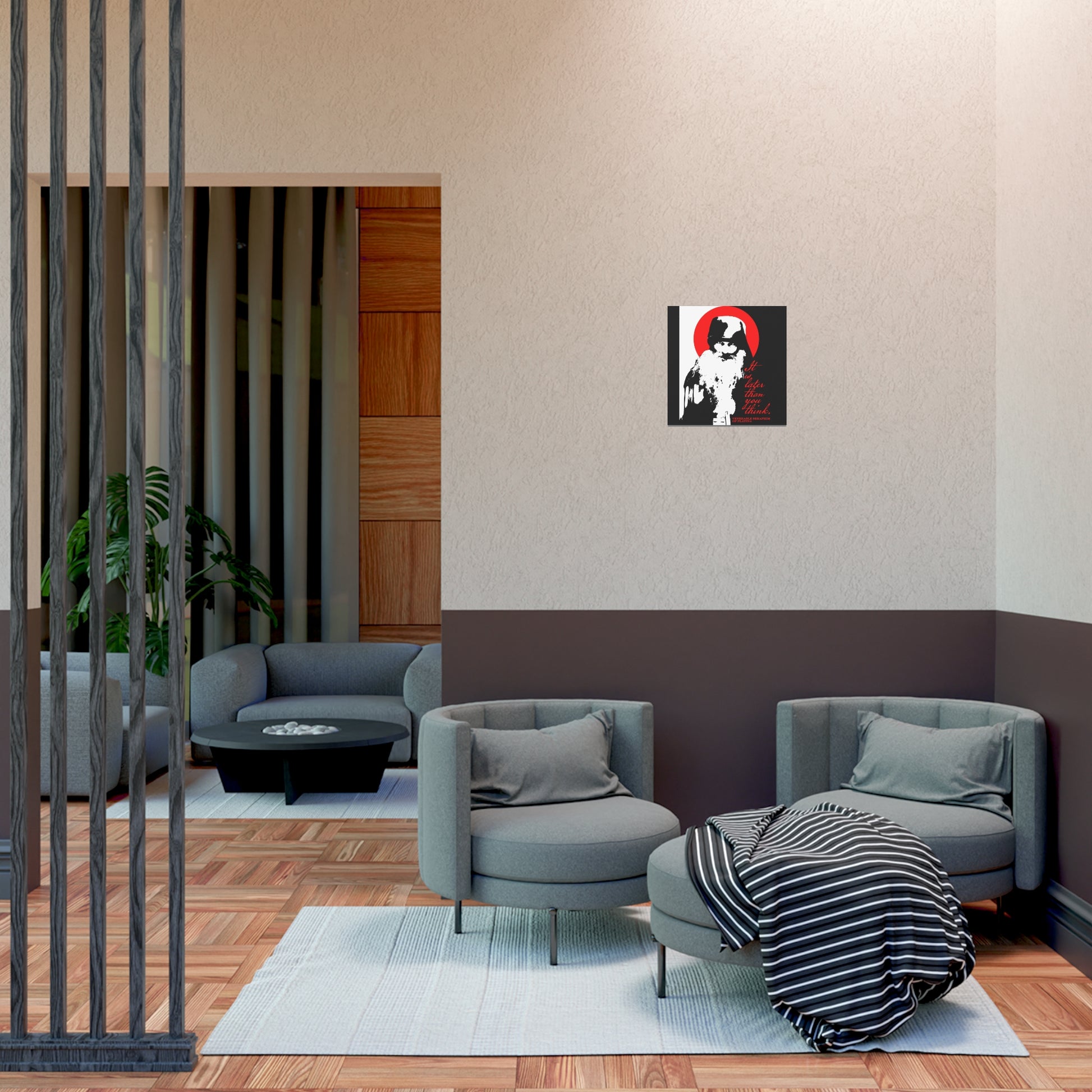 A modern lounge area features two gray armchairs, a round ottoman, and a striped blanket. The Remembrance of Death "It's Later Than You Think" Christian art poster by Fr Seraphim Rose and a plant create a tranquil, Orthodox-inspired setting.