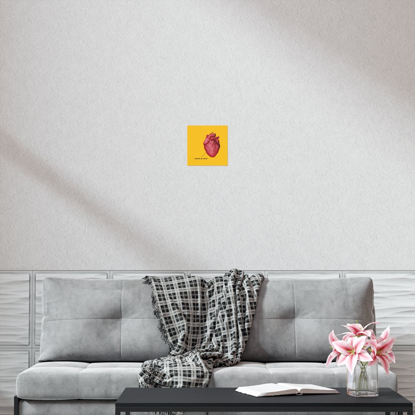 A gray sofa with a plaid throw, an open book on repentance, pink flowers, and a “Remember You Will Die” retro medical textbook heart Christian art poster with an Orthodox cross hang on the wall above.