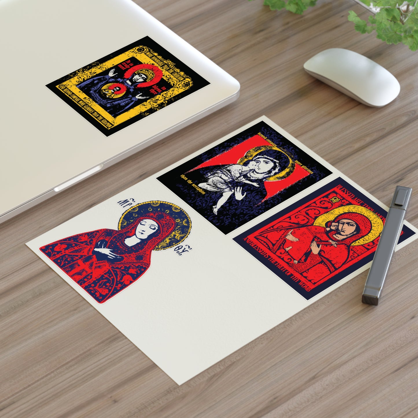 The Theotokos IconoGraphic Sticker Collection No. 1 by Remembrance of Death, featuring designs like the Vladimir Icon and "Joy of All Joys," is displayed on a desk with a pen, plant, mouse, and one Orthodox Christian sticker on a laptop.