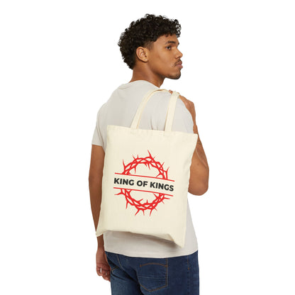 Man with curly hair holds a "King of Kings Crown of Thorns | The King of Glory | Christ is King | Revelation 19:16" Christian cotton canvas tote bag featuring a red crown of thorns graphic.