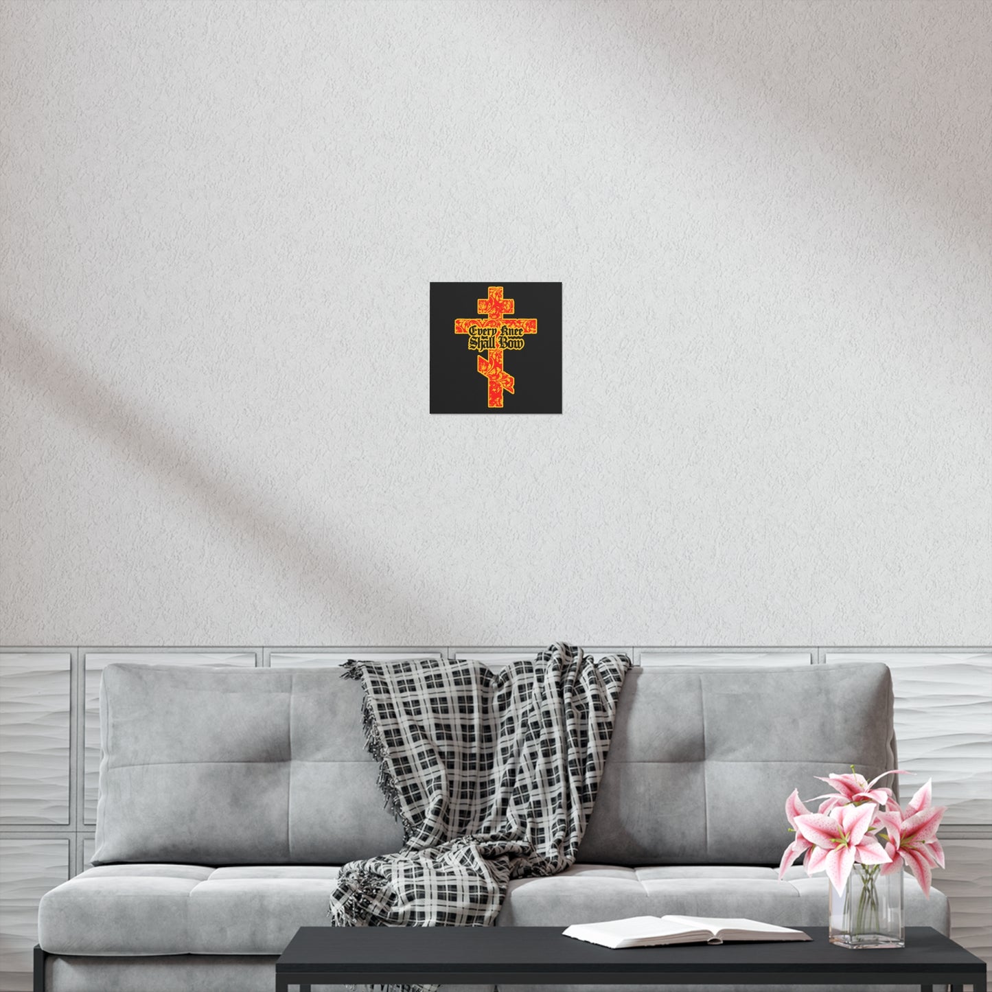 A gray sofa with a plaid throw, pink flowers, and an open book—opened to Isaiah 45:22-24—rests below the "Every Knee Shall Bow" gold and red Orthodox cross Christian art poster on a white wall.