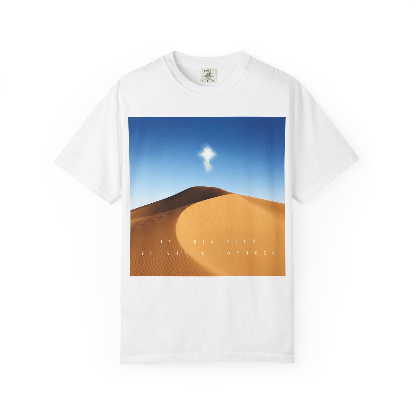 White "In This Sign Ye Shall Conquer Desert Sun Scene" heavyweight cotton unisex tee featuring a desert landscape with blue sky and a radiant cross above sand dunes, inspired by the Elevation of the Cross; "The Cross is the Might of Kings" text displayed at the bottom center.