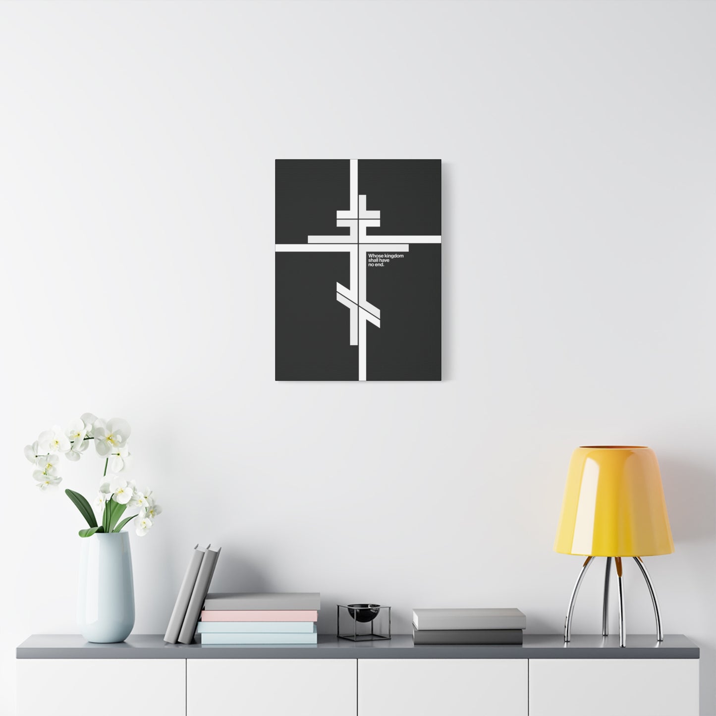 A modern room featuring the "Whose Kingdom Shall Have No End" Orthodox Cross canvas art, books, and a yellow lamp on a white cabinet reflects inspiration from Luke 1:32-33 and minimalist Christian design.
