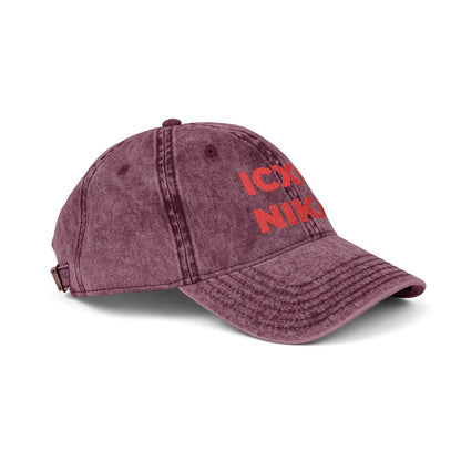 The Red ICXC NIKA Text Christogram distressed denim cap features red embroidered "ICXC NIKA" on maroon, symbolizing "Jesus Christ conquers," and displays the Orthodox Christian emblem from a side angle.