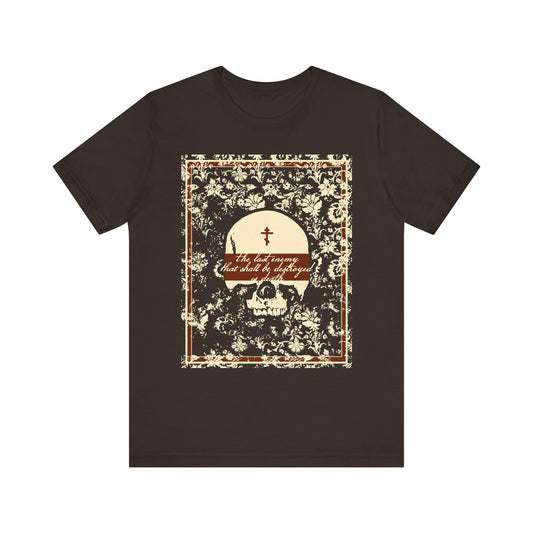 Brown t-shirt featuring an earthtone skull and floral design with ornate gothic frame, cross, and the text “The last enemy that shall be destroyed is death (1 Cor 15:26).” Inspired by the theme of victory over death from the Resurrection and Akathist to Jesus Conqueror. Lightweight cotton unisex fit.
