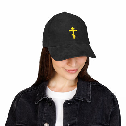 A woman smiles downward, quietly hopeful, wearing the Simple Yellow Orthodox TriBar Cross Embroidered Cotton Corduroy Cap—Orthodox Christian headwear known as a Weapon of Unseen Warfare Which Makes Demons Tremble.