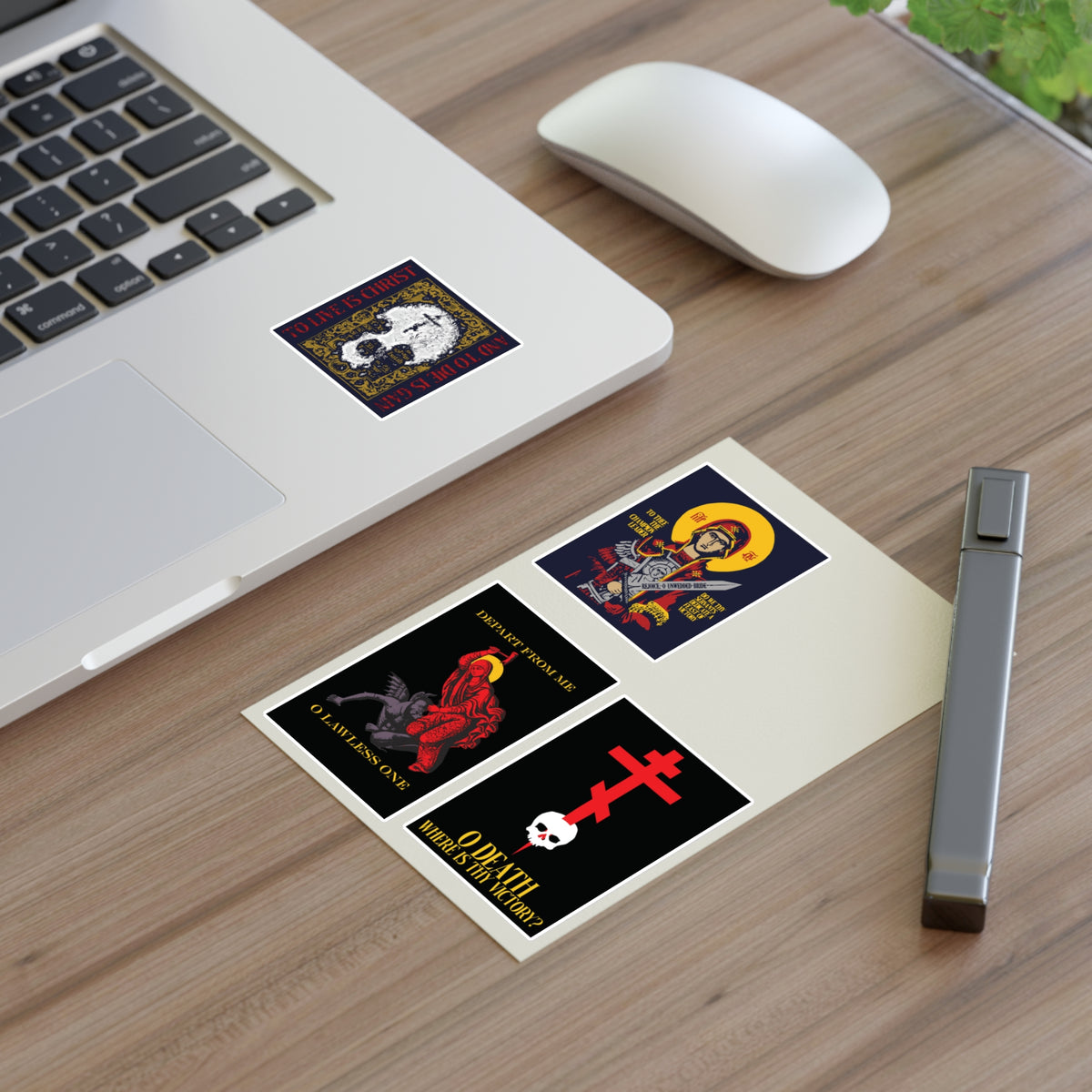Four vibrant Orthodox stickers from the “Bestseller Mix No. 1” set—including Theotokos Champion Leader, St Marina, Death Where is Thy Victory, and To Live is Christ—adorn a desk beside a laptop, pen, and mouse; perfect as unique Orthodox stickers or Theotokos icon stickers to add inspiration and meaning to your workspace.