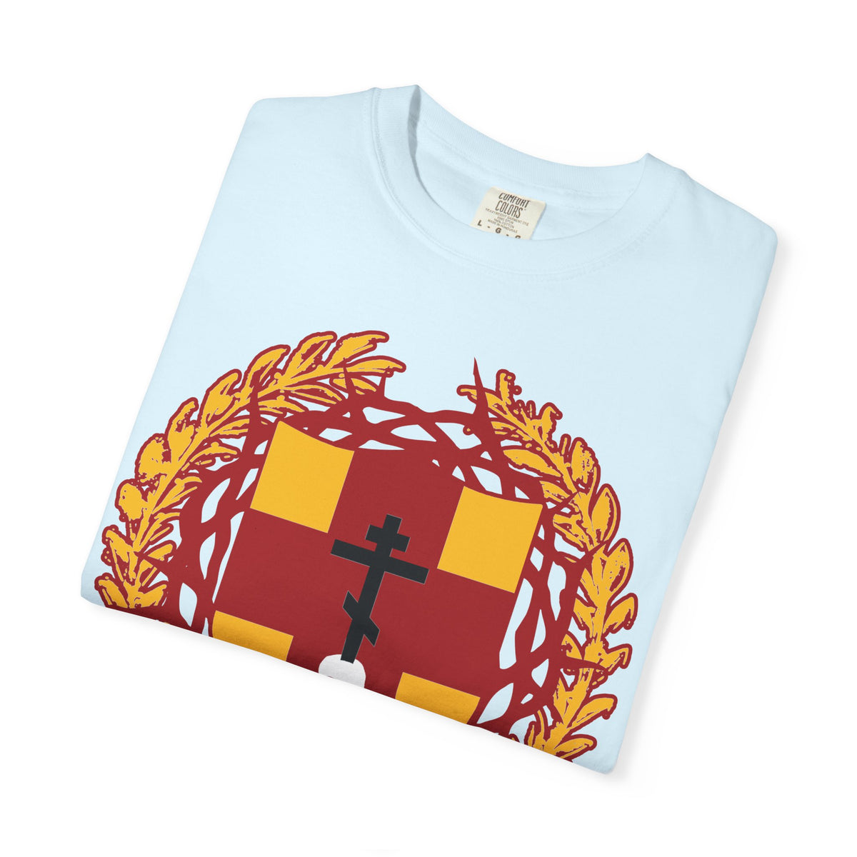 A folded light blue “First-Born from the Dead (Col 1:18)” heavyweight cotton t-shirt featuring a heraldic shield with a red and yellow crest, golden wreath, black Orthodox cross stabbing a skull, and crowned with thorns—a subtle reminder of redemption through His blood.