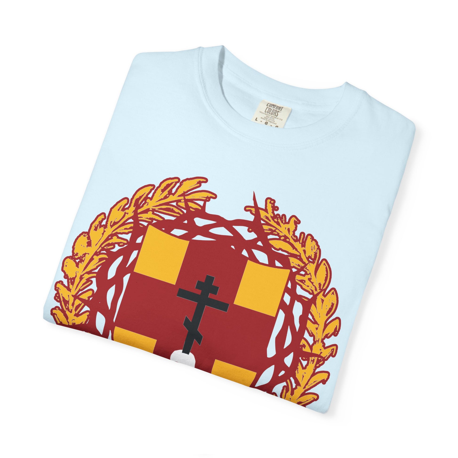 A folded light blue “First-Born from the Dead (Col 1:18)” heavyweight cotton t-shirt featuring a heraldic shield with a red and yellow crest, golden wreath, black Orthodox cross stabbing a skull, and crowned with thorns—a subtle reminder of redemption through His blood.