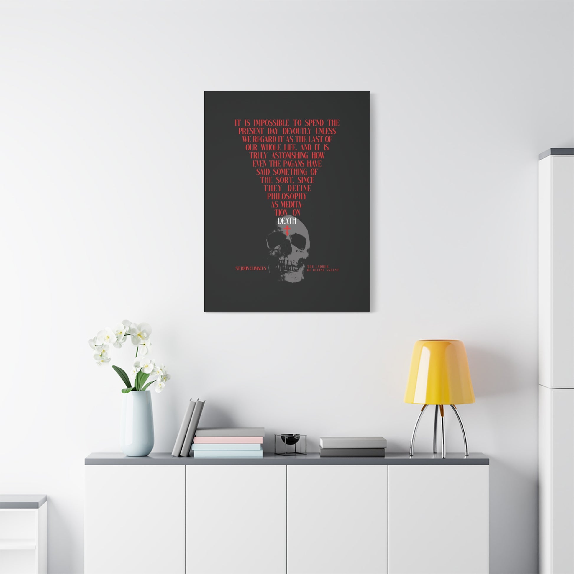 The "Present Day As the Last Day of Our Life" canvas, featuring a skull with a red Orthodox cross and memento mori theme, hangs above a white cabinet with plants and a yellow lamp.