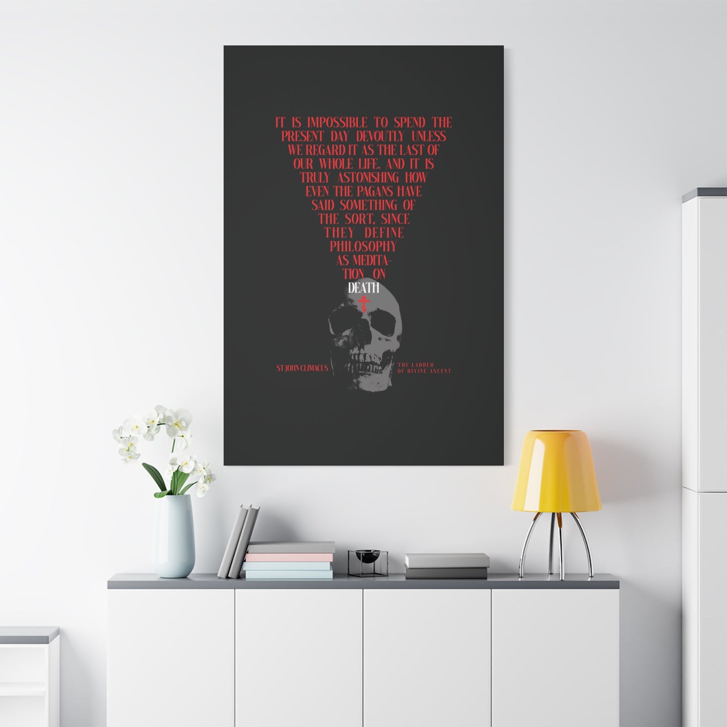 The Present Day As the Last Day of Our Life" Orthodox canvas wall art, featuring a skull with a red cross and inspired by St John Climacus’s memento mori meditation, displayed above a modern minimalist white cabinet, lamp, and flowers.