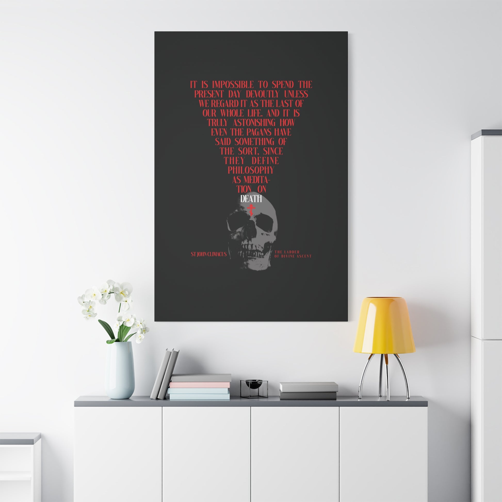 The Present Day As the Last Day of Our Life" Orthodox canvas wall art, featuring a skull with a red cross and inspired by St John Climacus’s memento mori meditation, displayed above a modern minimalist white cabinet, lamp, and flowers.