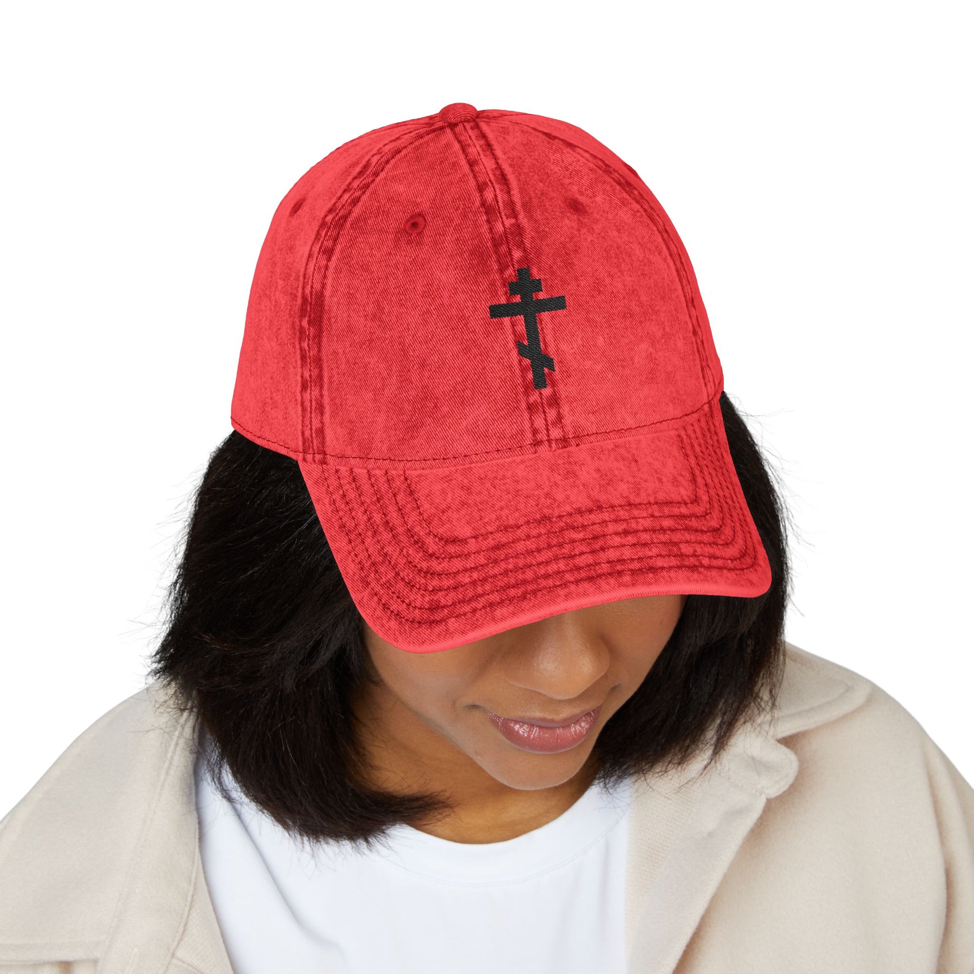 A woman looks down, wearing a white jacket and the Simple Black Orthodox TriBar Cross Cap—a minimalist, distressed embroidered cap with "Crucify My Ego to the Precious and Life Giving Cross" design.