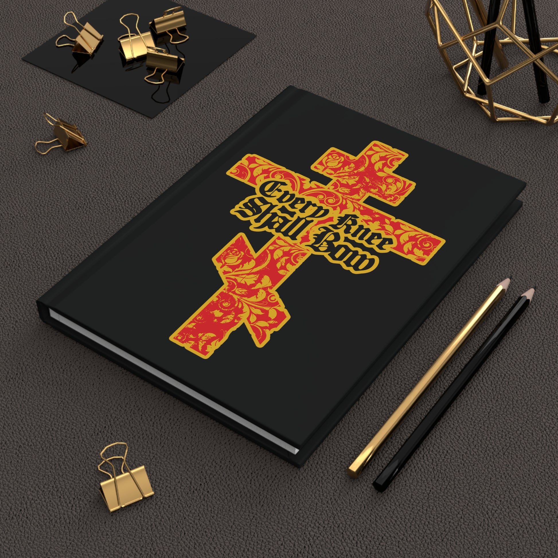 The "Every Knee Shall Bow" Christian Journal features a gold and red floral Orthodox cross with Gothic lettering (Isaiah 45:22-24, Phil 2:7-11) on a black cover, perfect for your desk or stationery collection.