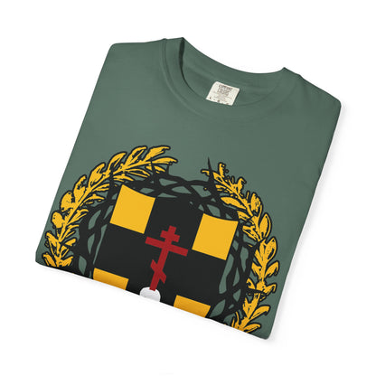 Folded green heavyweight cotton unisex t-shirt featuring a heraldic yellow-black shield with an Orthodox cross, red accents, gold laurel wreath, and crown of thorns—its bold design inspired by the message of “First-Born from the Dead” (Col 1:18), reflecting on redemption and salvation.