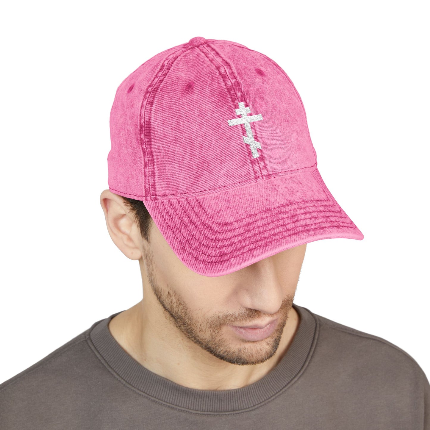 Man in a gray shirt looks down while wearing the Simple White Orthodox TriBar Cross Cap—minimalist Christian headwear with "Crucify My Ego to the Precious and Life Giving Cross" embroidered on a pink distressed hat.