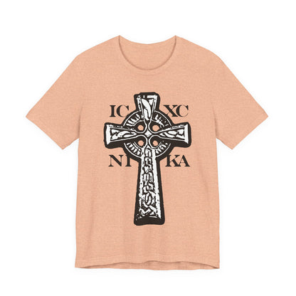 Heather Peach t-shirt featuring the ICXC NIKA Celtic Knotwork Cross in black and white on a red background, with "Jesus Christ Conquers"—a traditional Orthodox Christian design symbolizing salvation.