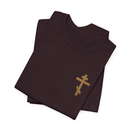 Small embroidered Orthodox cross in earthtones on a folded black Christian cotton unisex T-shirt with "May I Never Boast Except in the Cross (Gal 6:14)" displayed on a white background.