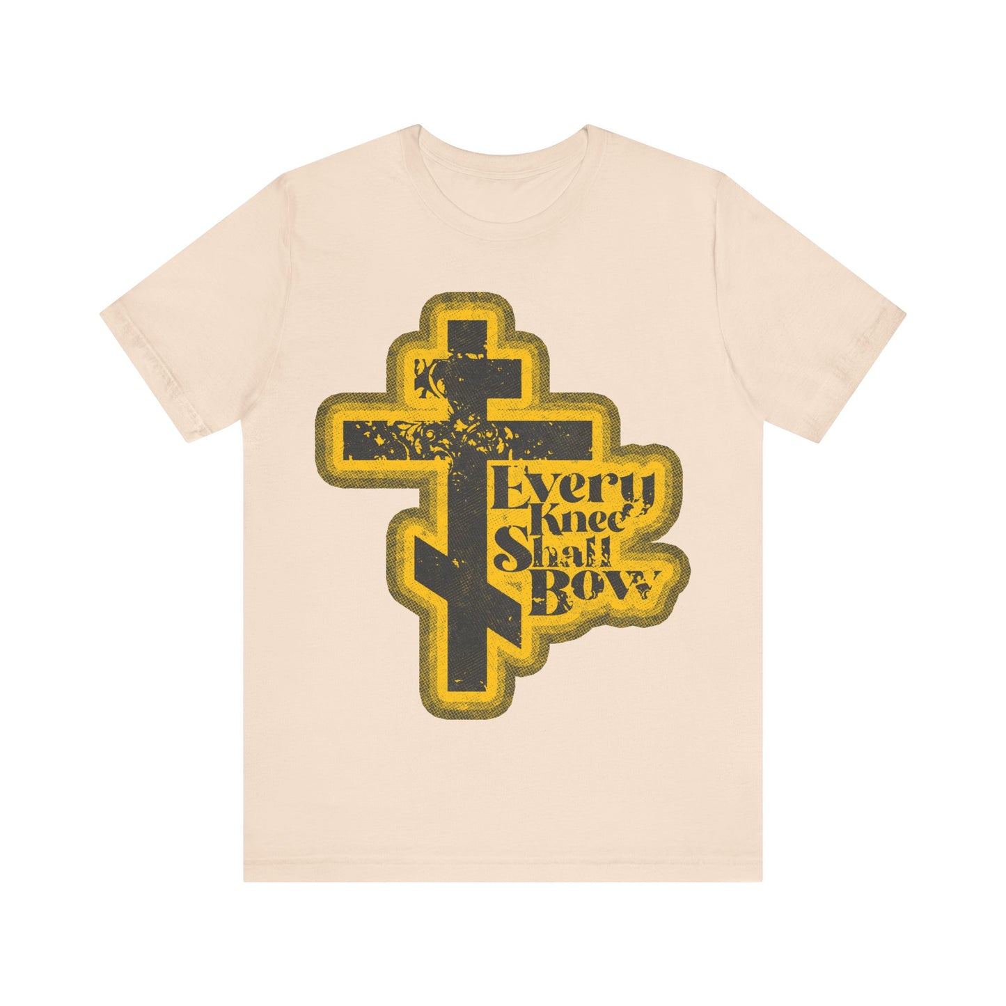Soft Cream t-shirt featuring a bold yellow and black cross graphic with "Every Knee Shall Bow," inspired by Philippians 2:10-11 & Isaiah 45:23, in a 70s distressed halftone comic book style. Orthodox Christian design.