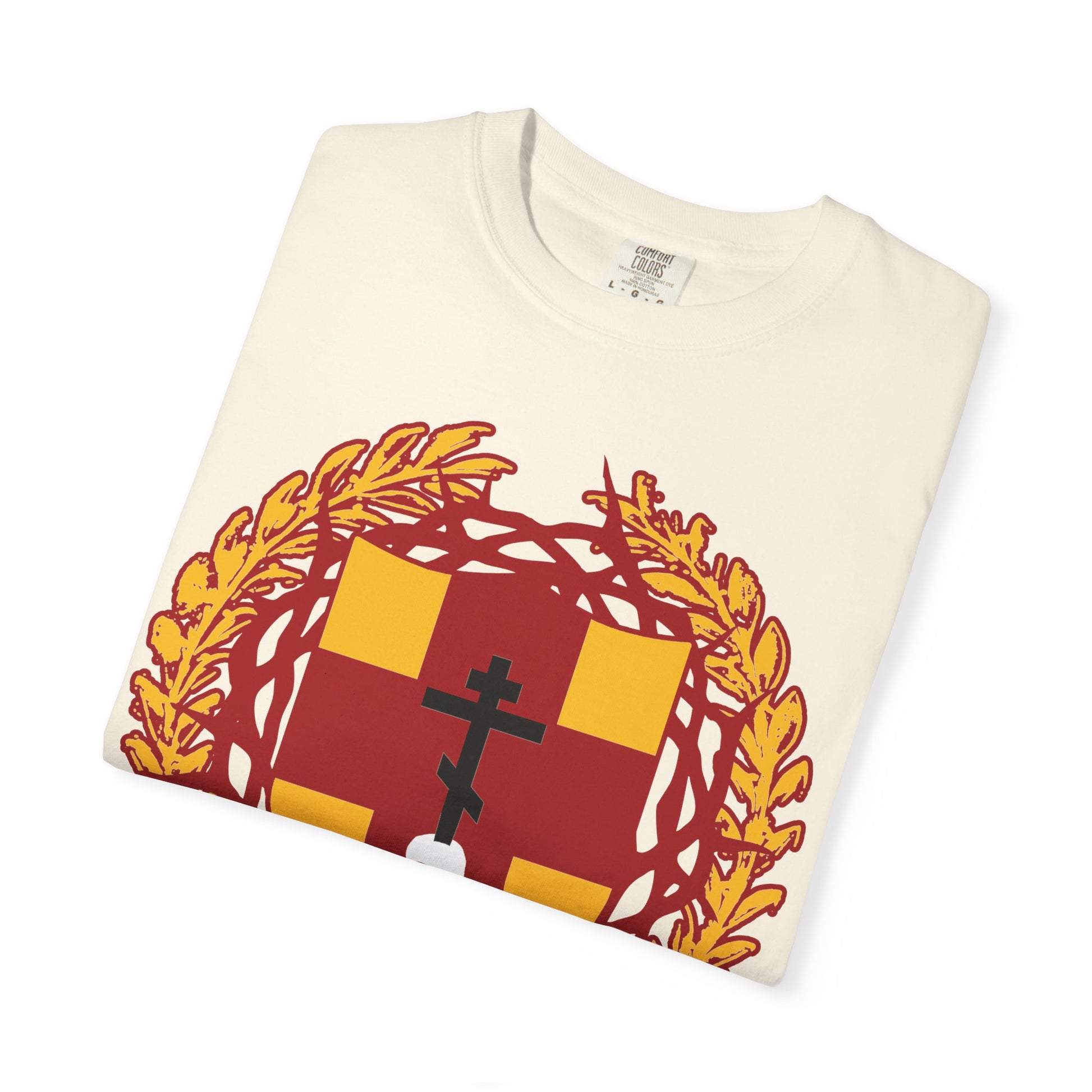 A folded white heavy cotton unisex t-shirt called “First-Born from the Dead (Col 1:18)” featuring a striking heraldic shield design: an Orthodox cross piercing a skull, crowned with thorns, and encircled by a bold yellow laurel wreath—imagery inspired by the biblical theme of redemption through His blood and the firstborn.