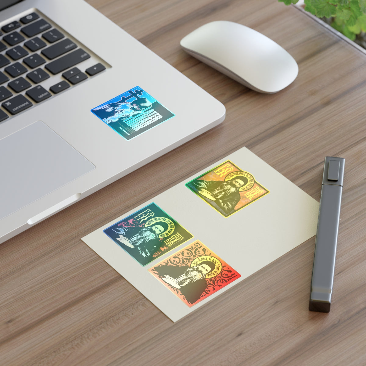 A laptop, mouse, pen, Fr Seraphim Rose Four Sticker Sheet No. 1, and green plant rest on a wooden desk.