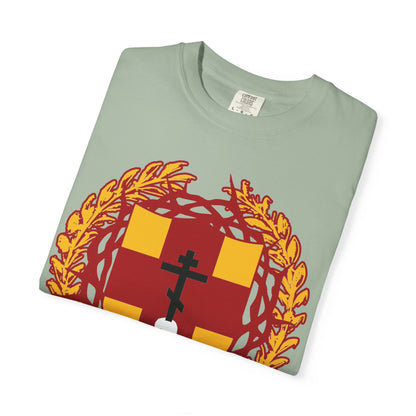 A folded light green heavyweight cotton unisex t-shirt titled “First-Born from the Dead (Col 1:18)” featuring an Orthodox Cross stabbing a skull, set on a heraldic shield adorned with a crown of thorns, inspired by redemption through His blood.