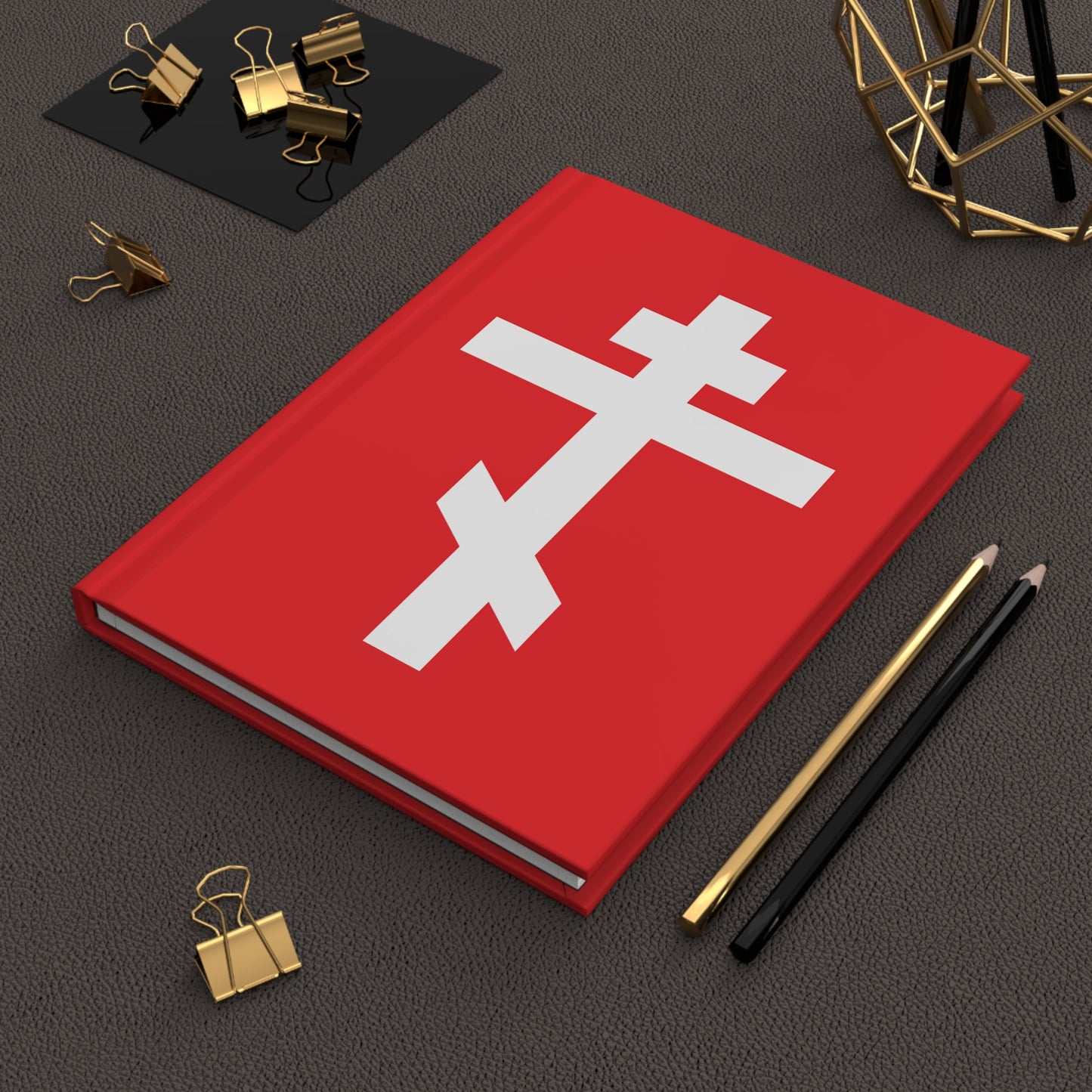 The "White Orthodox Cross Red Background" Orthodox Hardcover Journal features Gal 6:14 and is surrounded by pencils and gold binder clips. Inspired by St. John of Kronstadt, it has a red cover with a white Orthodox cross.