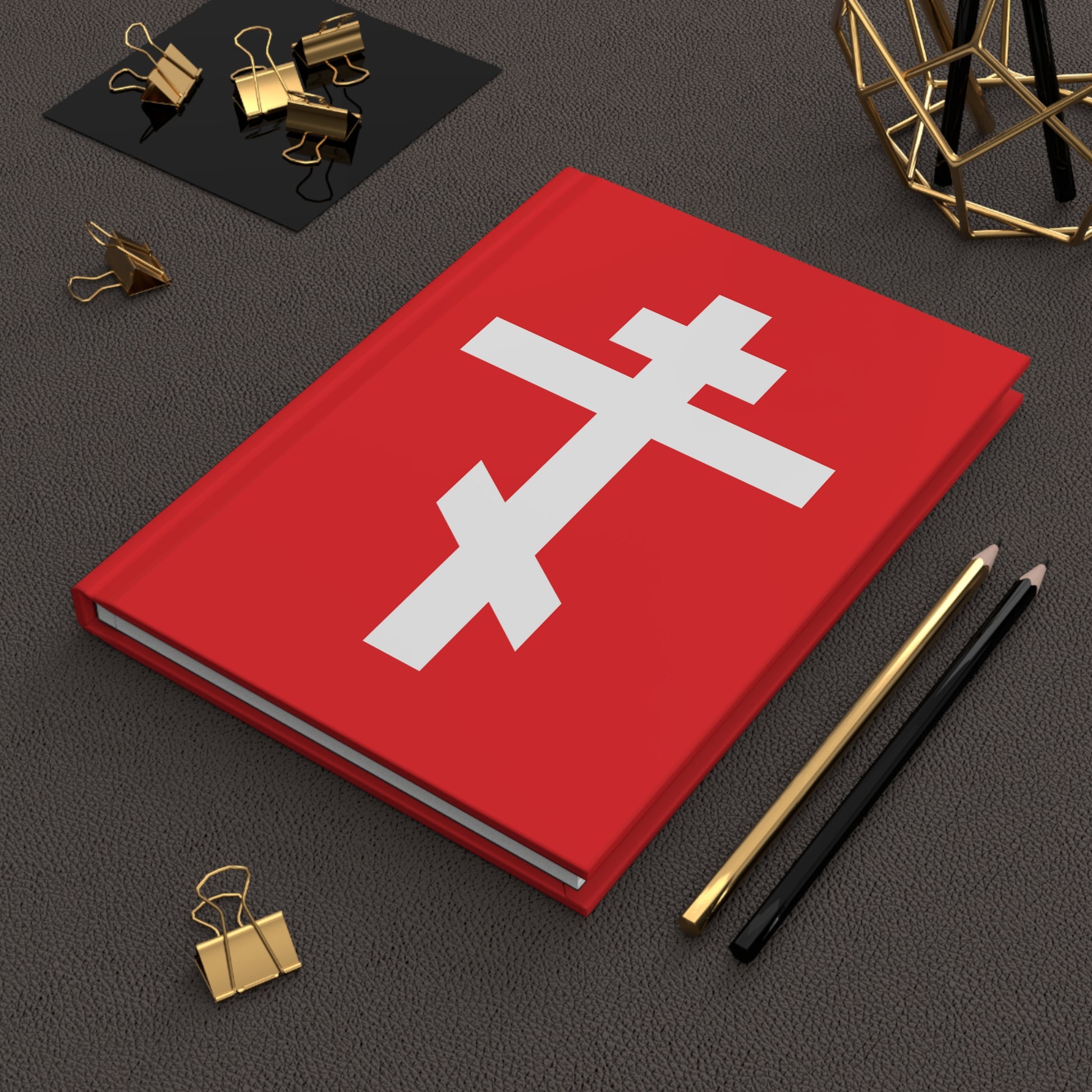 The "White Orthodox Cross Red Background" Orthodox Hardcover Journal features Gal 6:14 and is surrounded by pencils and gold binder clips. Inspired by St. John of Kronstadt, it has a red cover with a white Orthodox cross.
