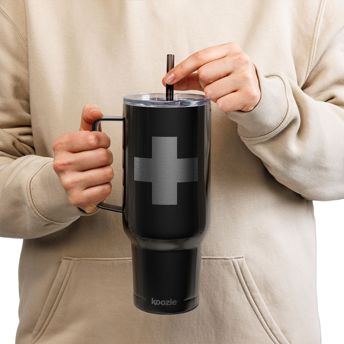 A person in a beige hoodie sips from a straw while holding the Minimalist Cross Engraved 40oz Koozie Tumbler—an insulated stainless steel Orthodox Christian home and travel accessory—featuring a simple cross design.