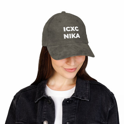 Woman in a dark jacket smiles, looking down, wearing the White ICXC NIKA Text Christogram Embroidered Cotton Corduroy Cap—an Orthodox Christian symbol meaning "Jesus Christ Conquers.
