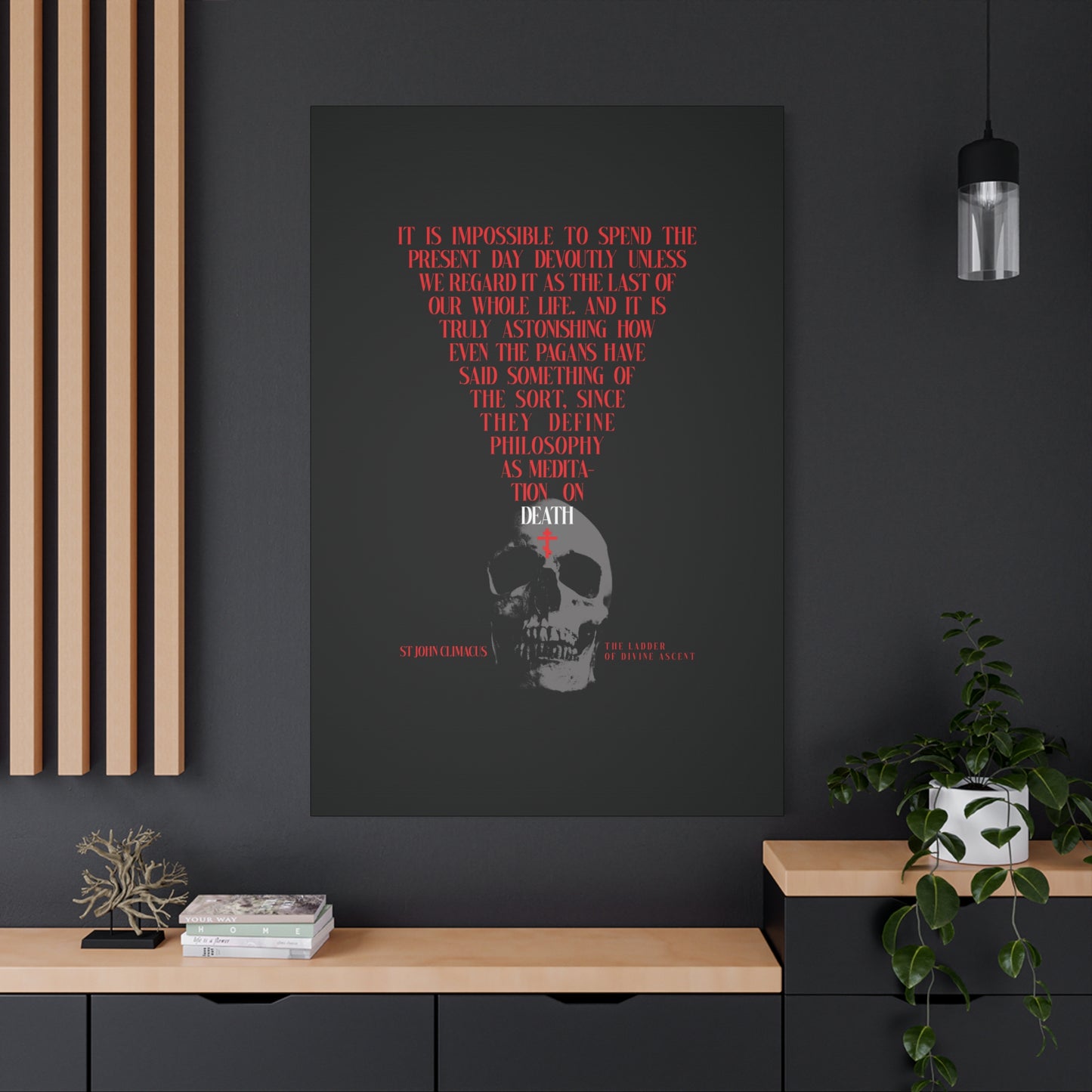 The Present Day As the Last Day of Our Life" Orthodox canvas wall art, featuring a skull with a red cross, hangs above a modern black and wood cabinet with plants on a gray wall.