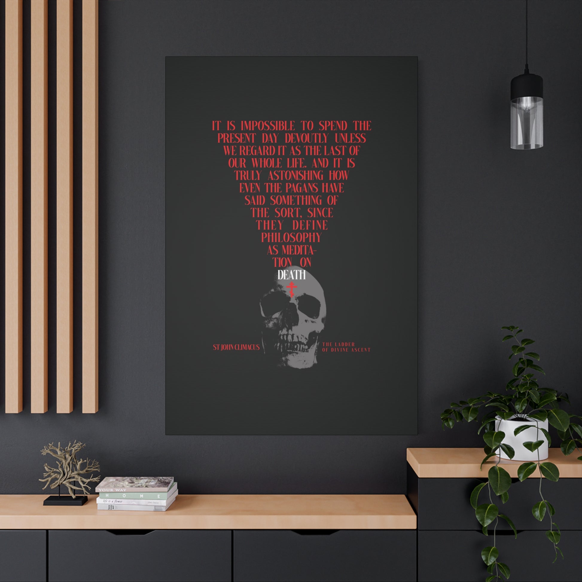 The Present Day As the Last Day of Our Life" Orthodox canvas wall art, featuring a skull with a red cross, hangs above a modern black and wood cabinet with plants on a gray wall.