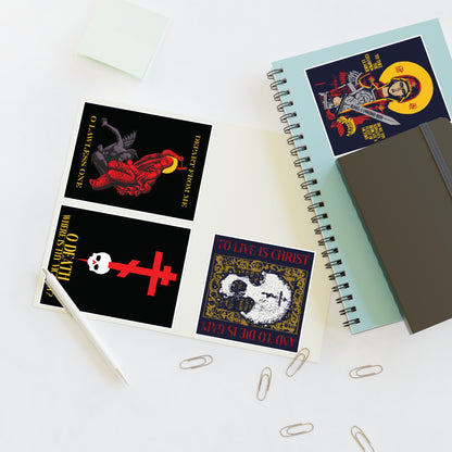 Open notebooks, paperclips, pen, sticky notes, and cards with dark religious-themed designs—featuring the Bestseller Mix No. 1: a set of four Orthodox stickers including Theotokos Champion Leader, St Marina, Death Where is Thy Victory, and To Live is Christ—are elegantly arranged on a white desk.