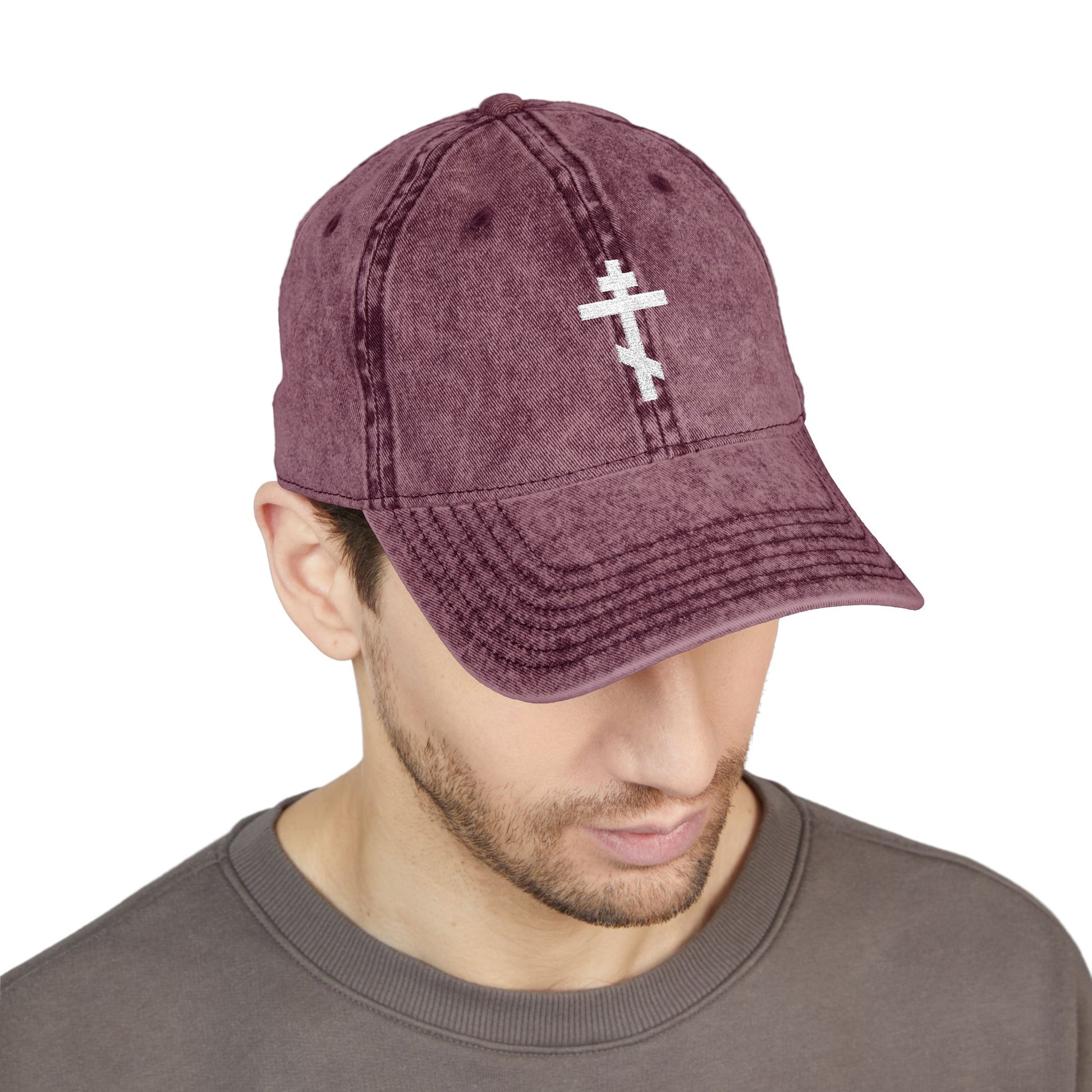 Man wearing the Simple White Orthodox TriBar Cross Minimalist Christian Distressed Embroidered Cap, looking down in a brown crewneck, reflecting on the Saviour’s sufferings.