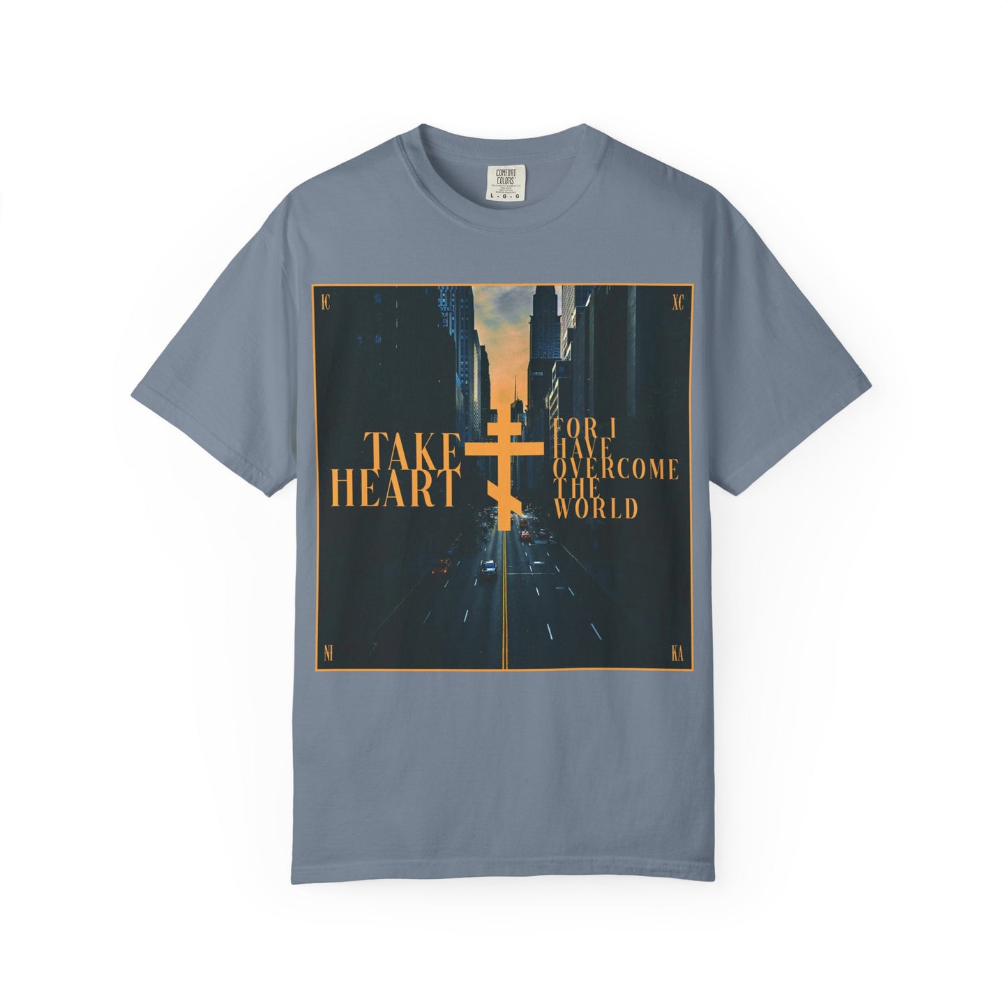Blue Jean heavyweight cotton unisex tee featuring a modern city street scene with a yellow Orthodox cross and the text: “Take heart, for I have overcome the world” (John 16:33)—a reminder that believers are promised joy in place of sorrow.