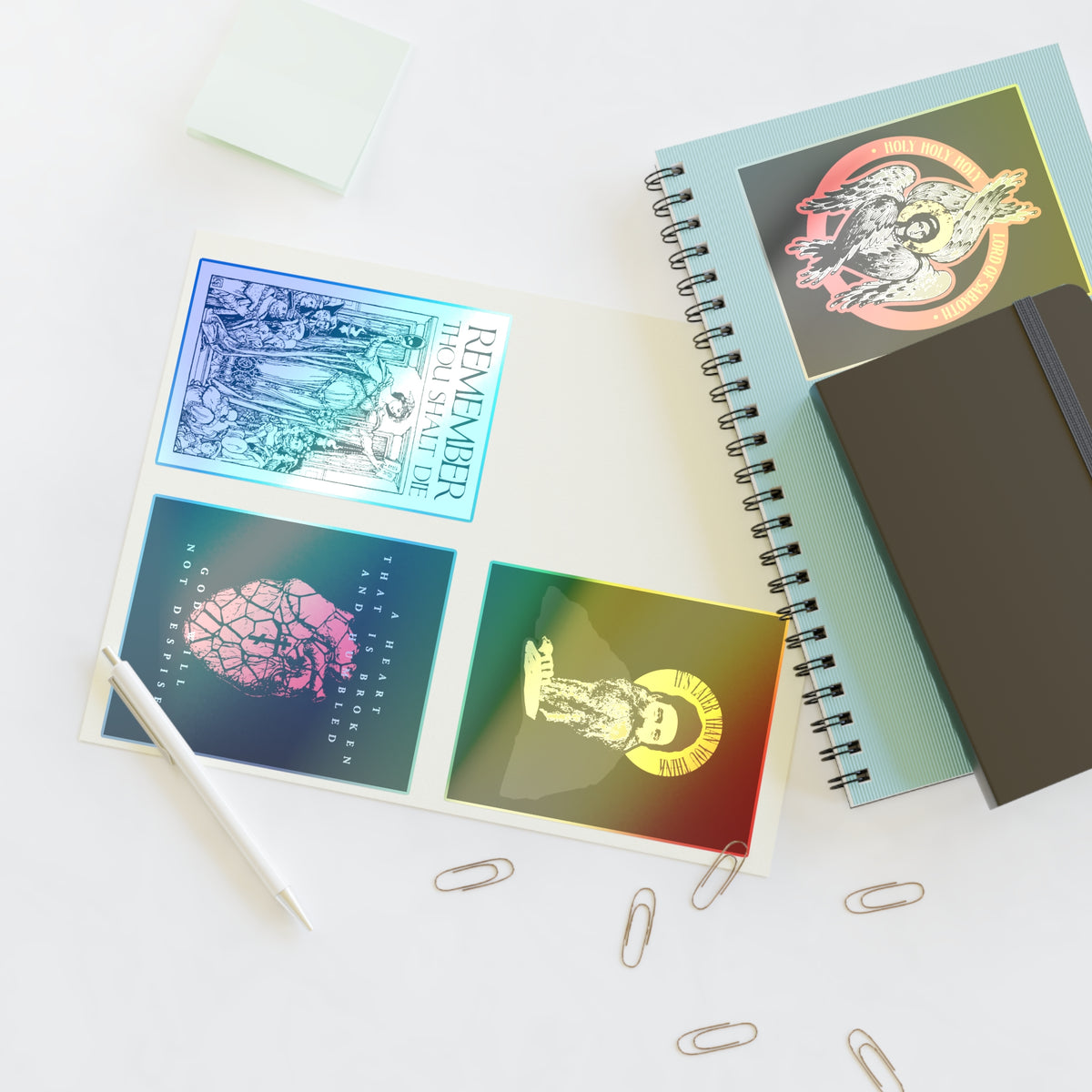 Open notebook with Bestseller Orthodox Sticker Mix No. 4, pen, clips, sticky notes, and a Memento Mori spiral notebook.