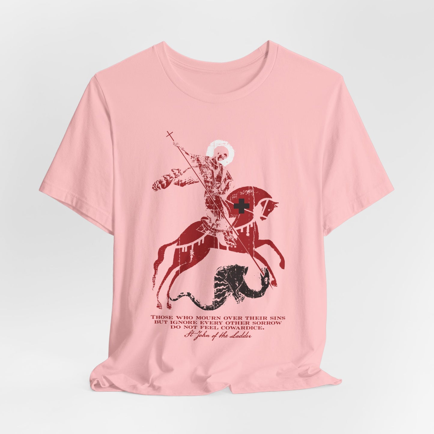 A pink unisex lightweight cotton t-shirt featuring a graphic of St George slaying the dragon, with black cursive text below inspired by St John Climacus’s teachings on mourning over one’s sins.