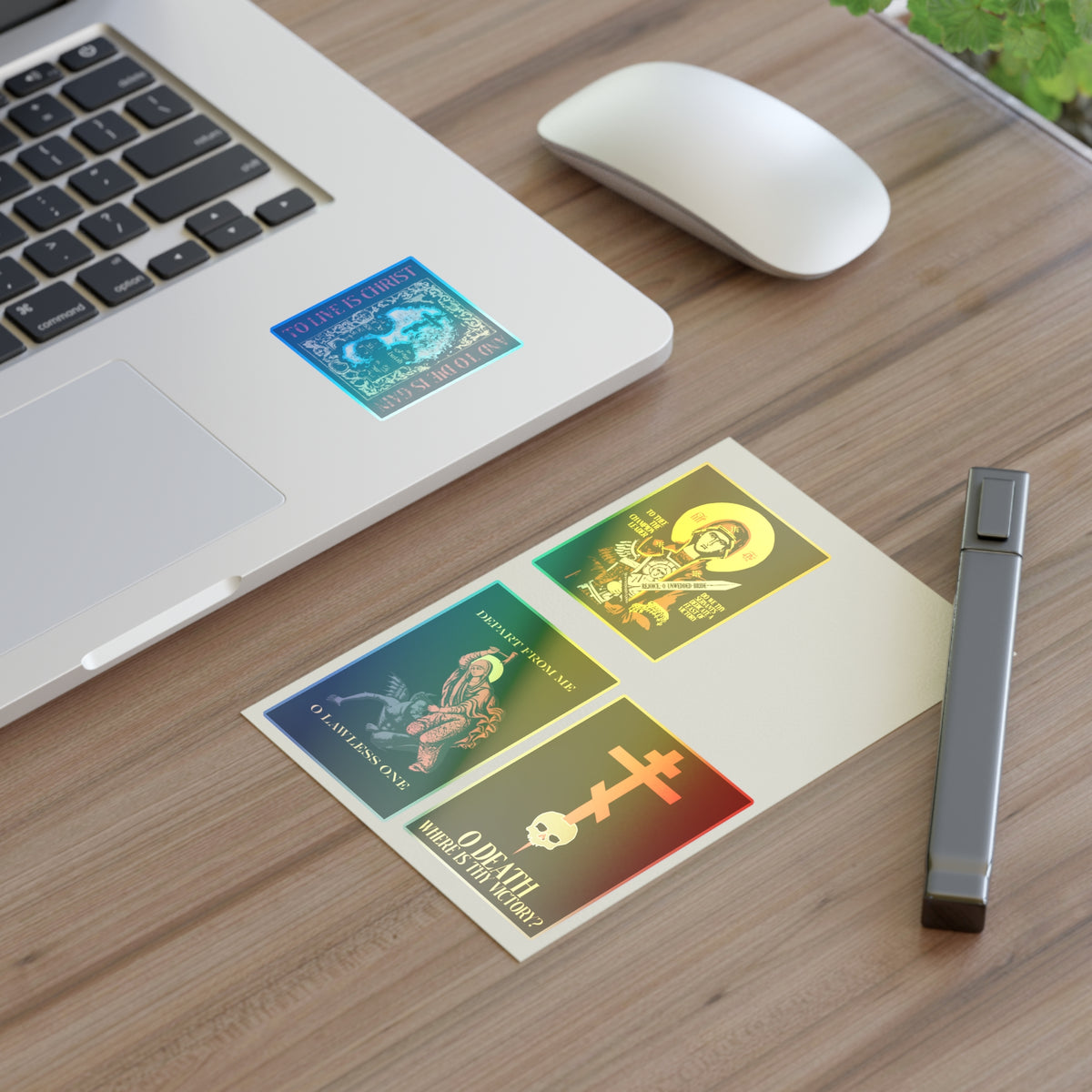 A laptop, mouse, pen, and a card decorated with the Bestseller Mix No. 1 Four Orthodox Stickers—including Theotokos Champion Leader, St Marina, Death Where is Thy Victory, and To Live is Christ—sit on a wooden desk.