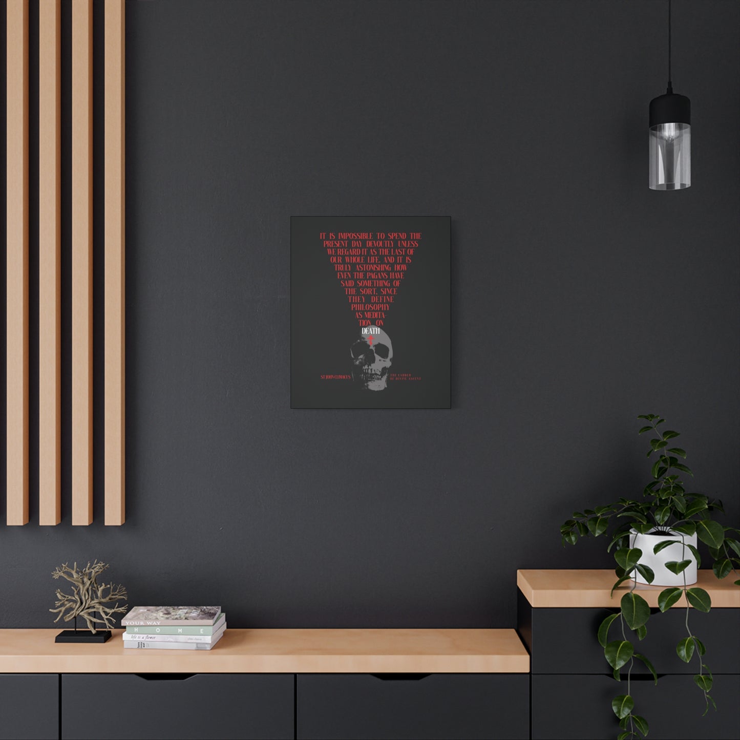 A modern black wall features "The Present Day As the Last Day of Our Life" Orthodox Canvas Wall Art, with a Skull and Red Cross by St John Climacus, surrounded by books, a plant, and minimalist decor—inviting mindful meditation on life and mortality.