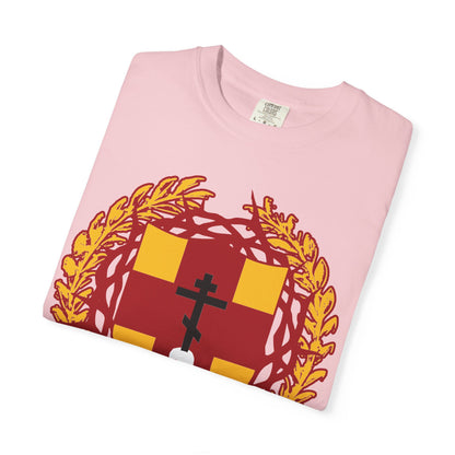 A folded pink heavyweight cotton unisex t-shirt featuring a heraldic shield with an Orthodox cross stabbing a skull, crowned with thorns, inspired by the “First-Born from the Dead” (Col 1:18) Bible verse and the theme of redemption through His blood.